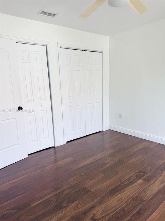 Wood-finish flooring, white walls, two panel doors, bi-fold closet doors, and a ceiling fan