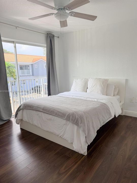 Dark wood-finish flooring, sliding glass door, overhead ceiling fan with light, white walls, and a white balcony railing
