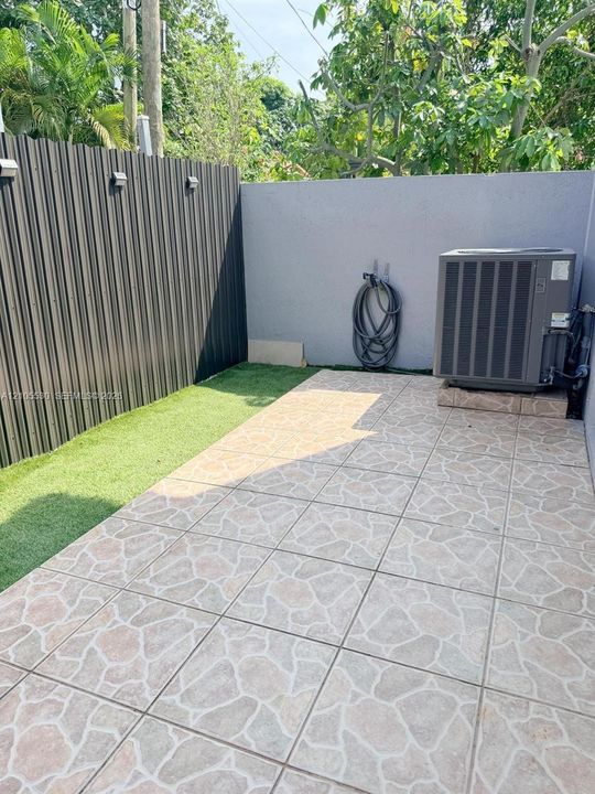 Paved patio area featuring patterned floor tiles, artificial turf, and a corrugated metal fence