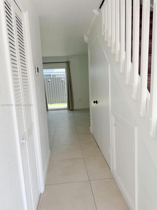 Tile flooring, white louvered bifold doors, white interior doors, white staircase balusters, and a sliding glass door