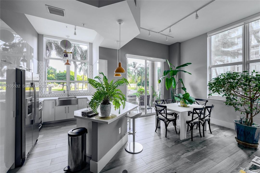 Kitchen featuring wood-finish flooring, quartz-surfaced island, stainless steel farmhouse sink, and high-reaching windows