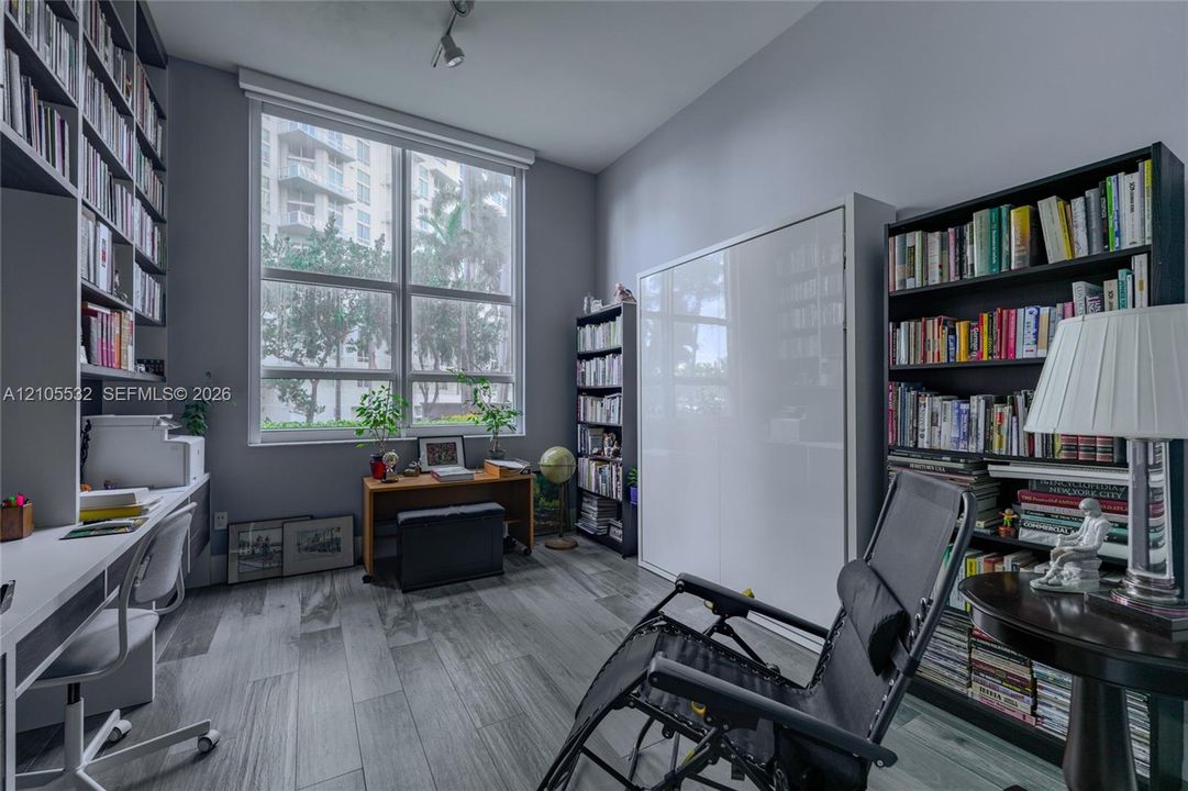 Large picture window with natural illumination, built-in floor-to-ceiling shelving, wall-integrated cabinetry, and wood-finish flooring