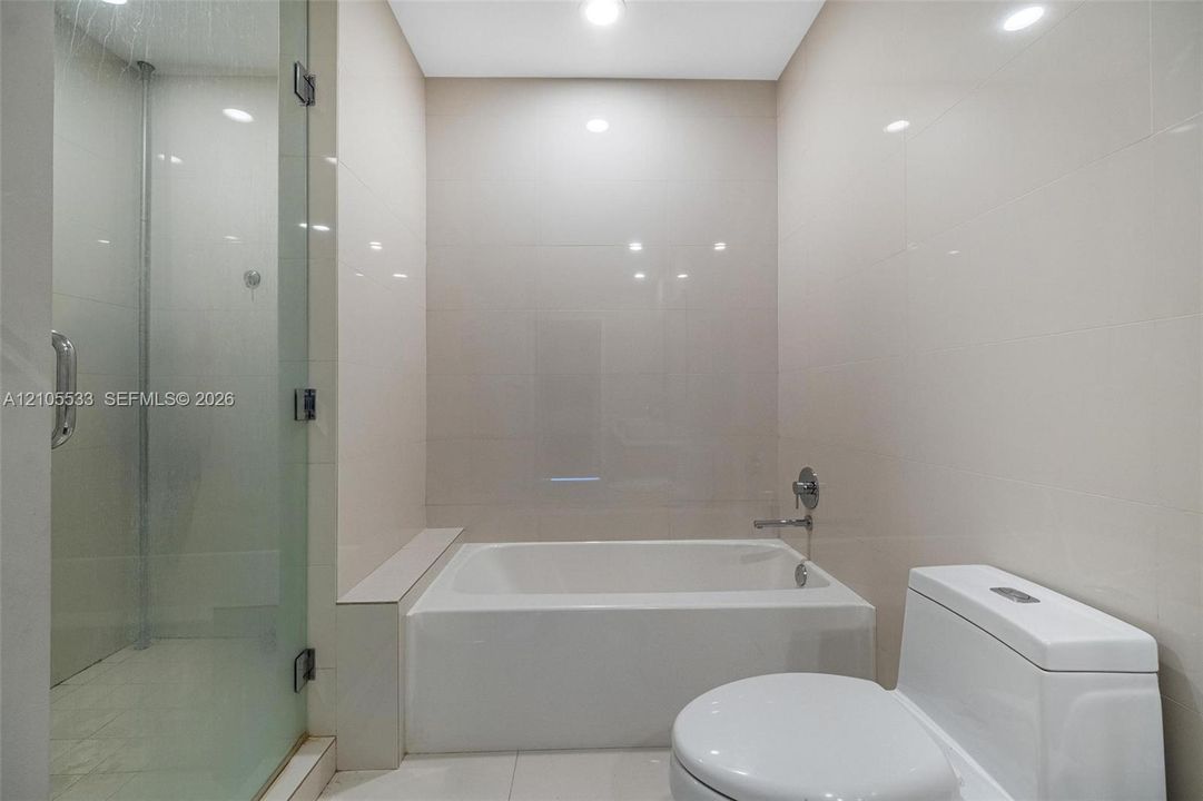 Bathroom featuring a separate glass-enclosed shower, built-in soaking tub with a deck, and large-format tile wall cladding