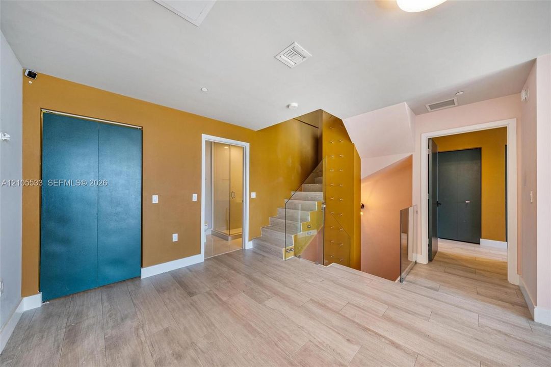Interior featuring wood-finish flooring, staircase with glass panel railing, and built-in closet with double-panel doors