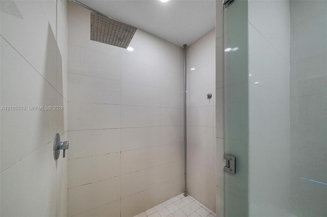 Walk-in shower featuring large-format ceramic wall tile, square rainfall showerhead, glass door enclosure, and lever-style plumbing fixture