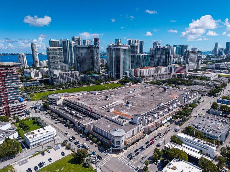 Aerial perspective of a multi-level commercial complex featuring integrated parking facilities, ground-level retail spaces, and a prominent corner architectural tower