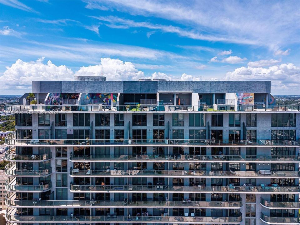 High-rise residential exterior featuring expansive floor-to-ceiling windows, wrap-around glass balconies, and a rooftop terrace level