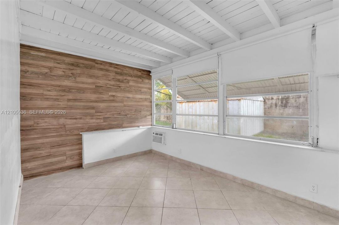 Exposed ceiling beams, wood-finish accent wall, tile flooring, and oversized horizontal windows