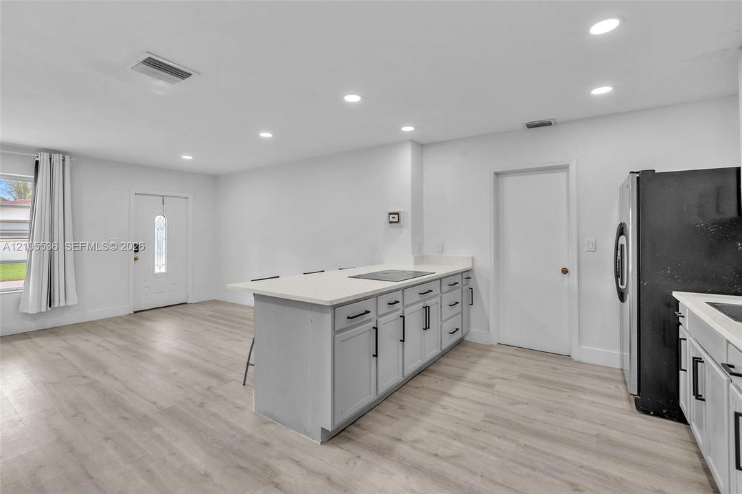 Kitchen featuring an island with a light-toned countertop, shaker-style cabinetry with matte black hardware, recessed lighting, and wood-finish flooring