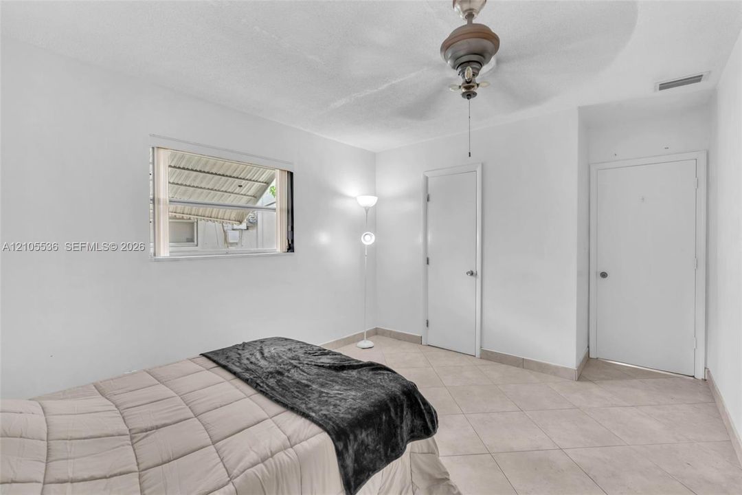 Neutral-toned tile flooring, white interior walls, ceiling fan, and window featuring horizontal louvers