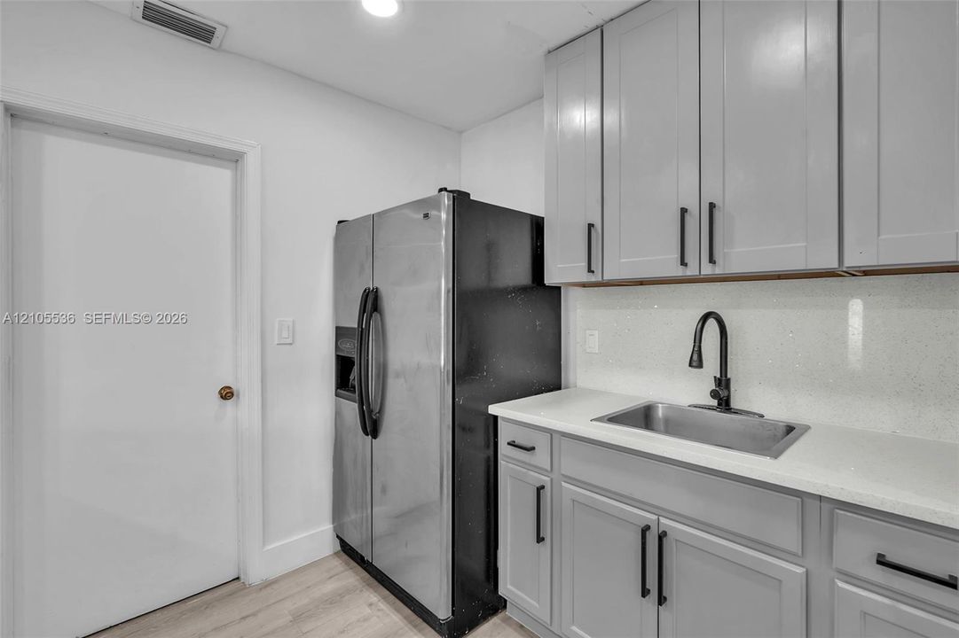 Grey shaker-style cabinetry with matte black hardware, stone-surface countertop, stainless steel sink, matte black gooseneck faucet, and wood-finish flooring