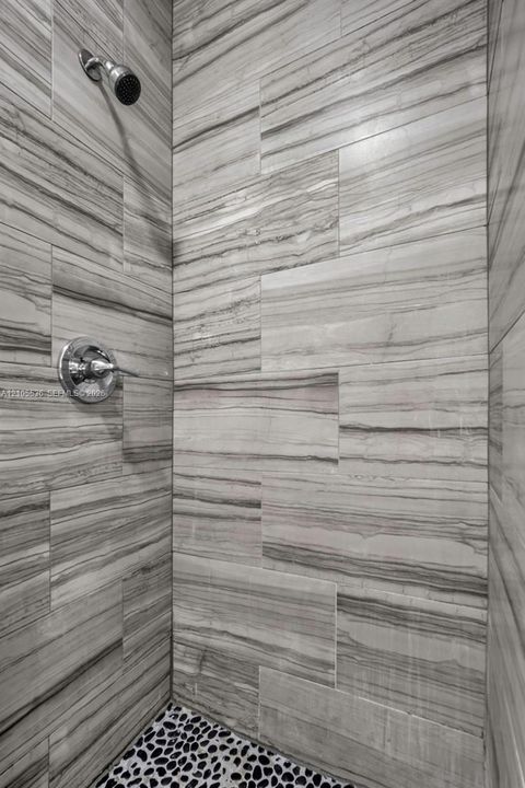 Shower enclosure featuring large-format linear-patterned wall tile, polished chrome shower head, matching chrome temperature control valve, and pebble-textured floor tile