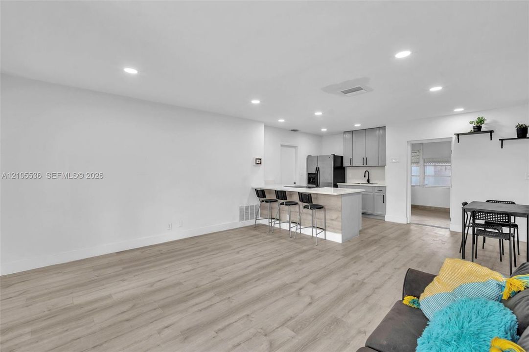 Open-concept kitchen featuring light grey cabinetry, stone-finish countertops, an integrated breakfast bar, recessed lighting, and wood-finish flooring throughout
