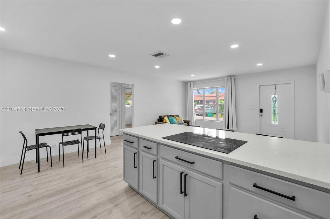 Kitchen island featuring light-toned cabinetry, quartz countertops, and a flush-mount electric cooktop, complemented by wood-finish flooring and recessed lighting