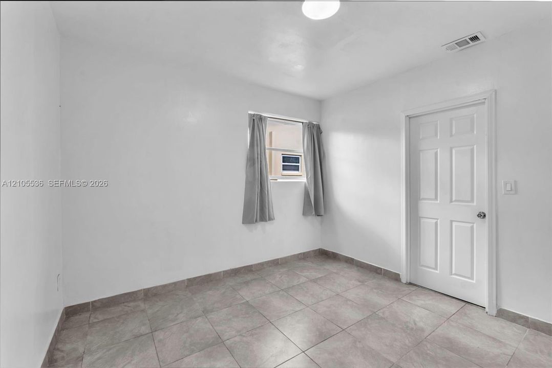 Neutral interior space featuring tile flooring, a single window, and a six-panel door
