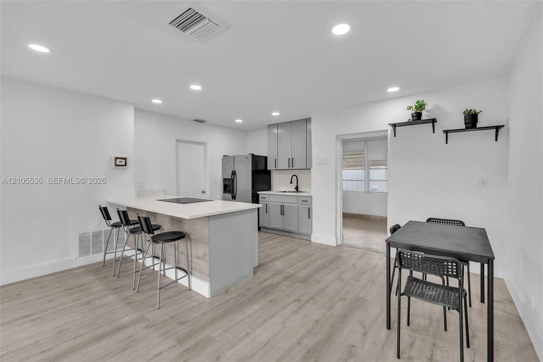 Kitchen featuring wood-finish flooring, gray shaker-style cabinetry, a stone-surface breakfast bar, recessed lighting, and stainless steel appliances