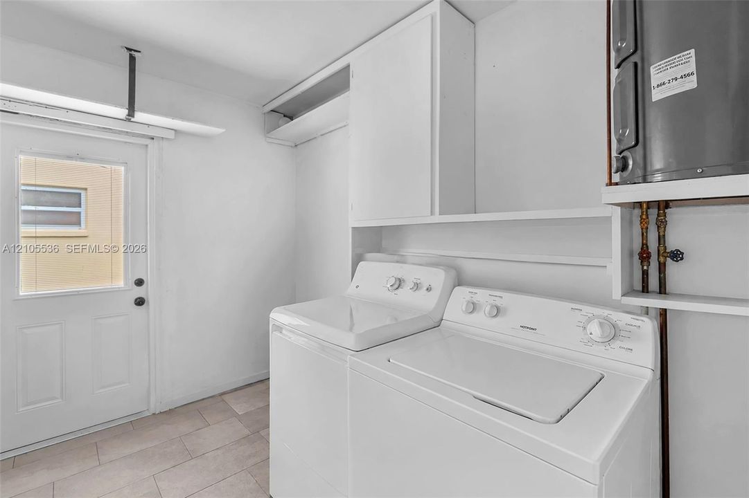 Utility space featuring tile flooring, built-in overhead cabinetry, open shelving, and an exterior door with an inset window