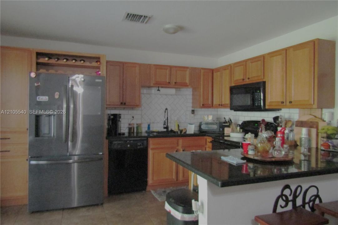 Kitchen featuring wood cabinetry, a built-in wine rack, stainless steel refrigerator, black appliances, and a dark stone countertop on the island