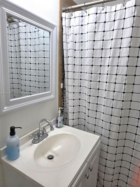 Vanity with integrated sink and chrome faucet, framed mirror, and tiled shower surround