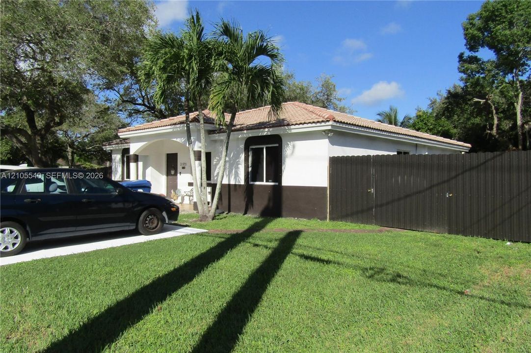 Manicured front lawn with mature trees, a paved driveway, and a privacy fence