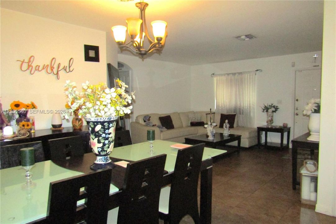 Open concept living and dining areas featuring dark wood-finish flooring, a decorative archway, and a chandelier light fixture
