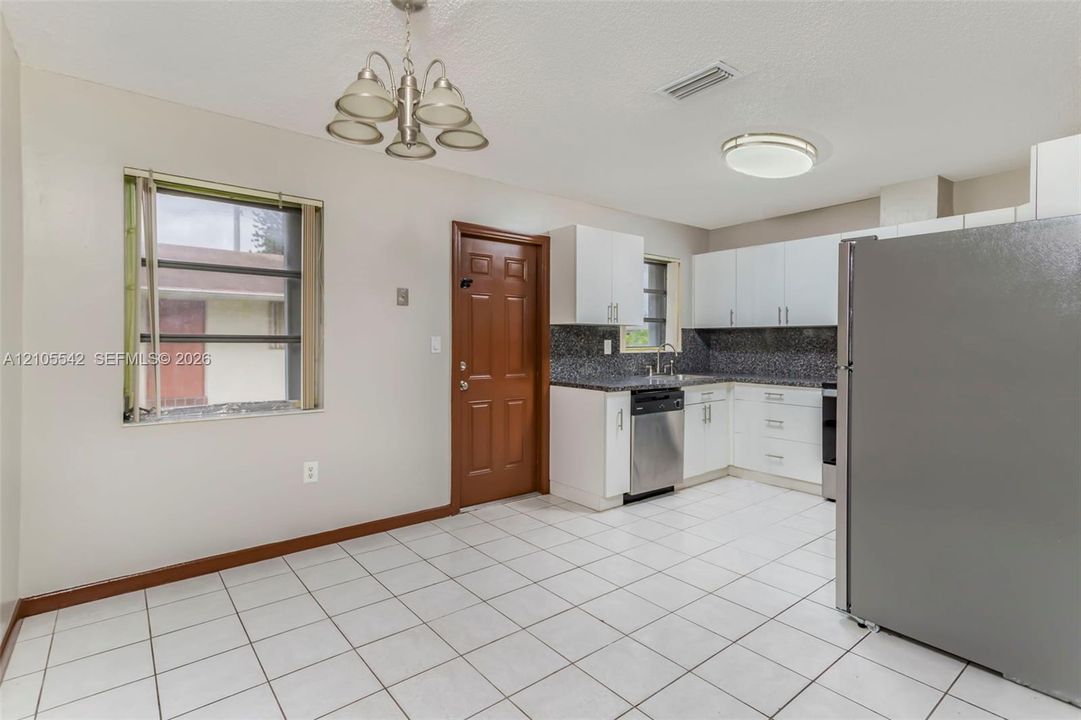 Tile flooring, white cabinetry, granite-finish countertops, stainless steel appliances, and a brown paneled door