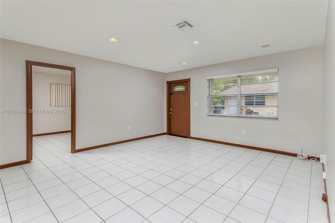 White tile flooring, recessed lighting, and a wood-finish entry door with clear glass panel