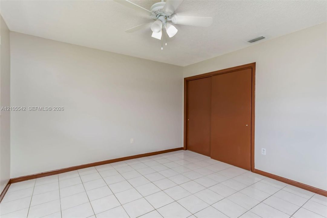 White tile flooring, light neutral wall paint, ceiling fan light fixture, and brown sliding closet doors