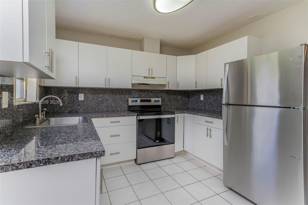 White cabinetry, stainless steel appliances, dark speckled countertops, tile backsplash, and a stainless steel sink with a gooseneck faucet