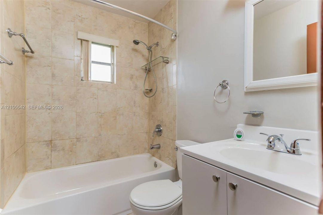 Full bathroom featuring a white vanity with integrated sink, chrome faucet, tiled shower surround, and a fixed window