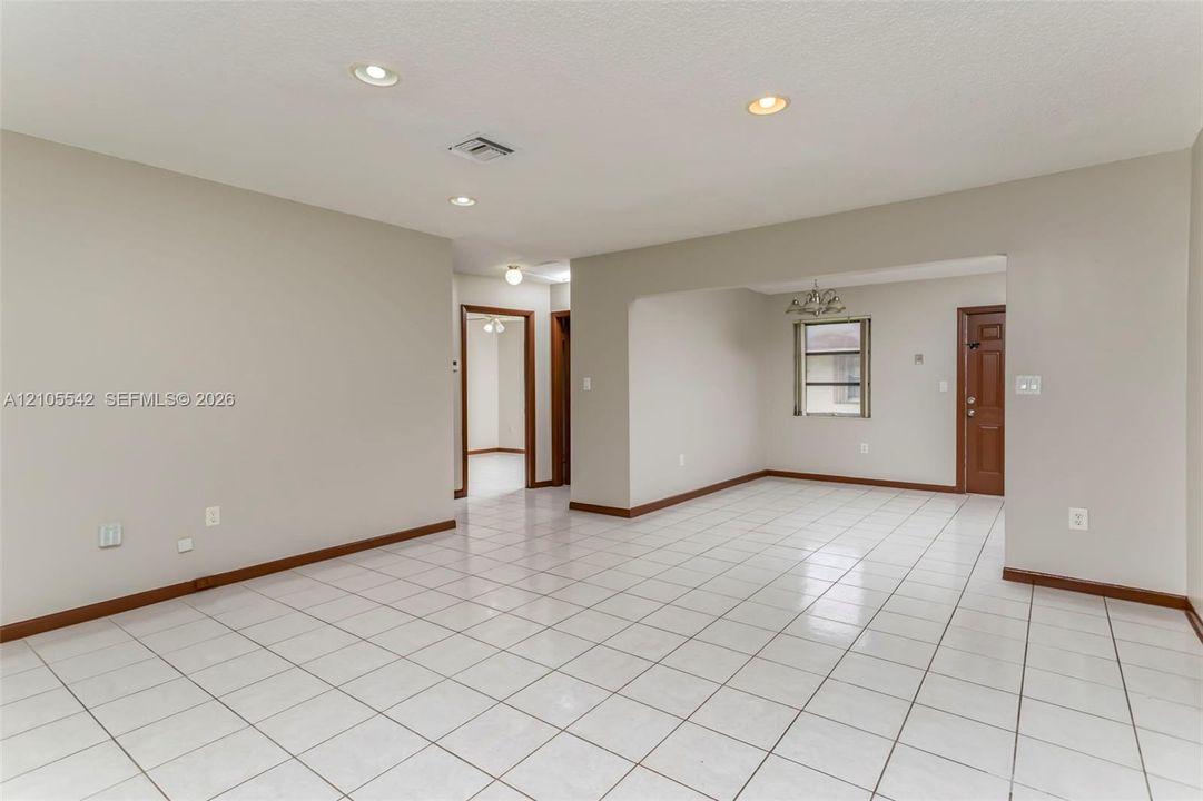 Spacious room featuring white tile flooring, recessed lighting, neutral wall tones, and wood-finish trim
