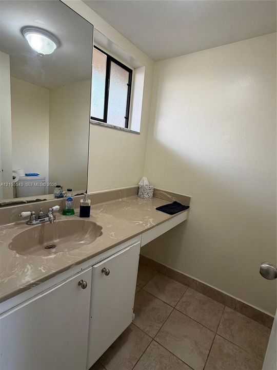Bathroom featuring a vanity with a solid-surface countertop, integrated basin, large wall-mounted mirror, ceramic tile flooring, and a window with privacy glass