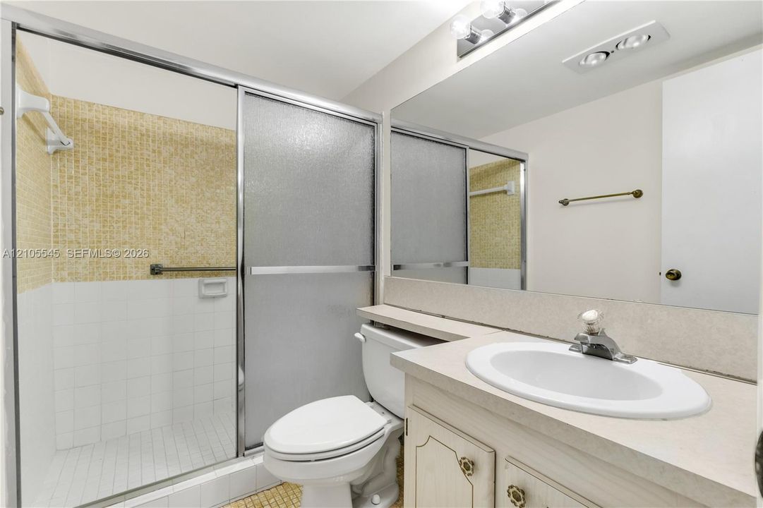 Shower enclosure with sliding frosted glass doors, a vanity with an integrated sink and base cabinetry, and a full-width mirror