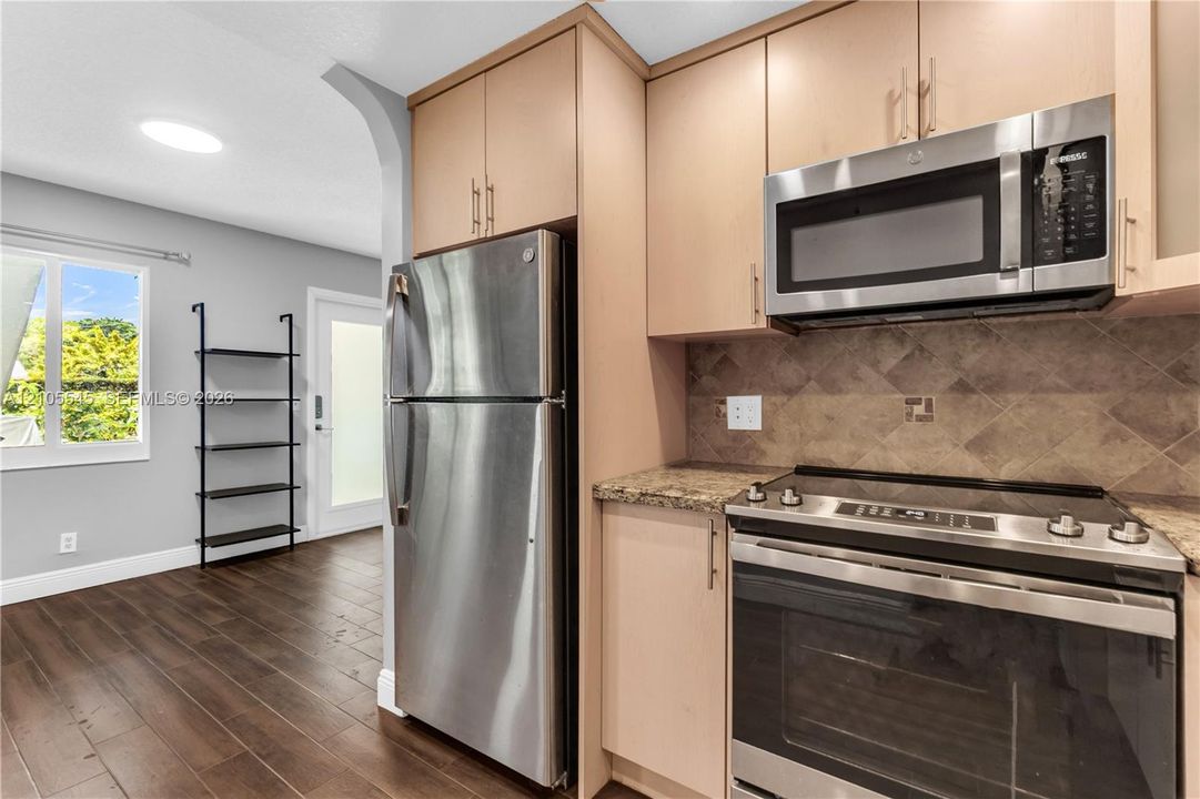 Kitchen featuring stainless steel appliances, wood-finish cabinetry, a patterned tile backsplash, and stone countertops