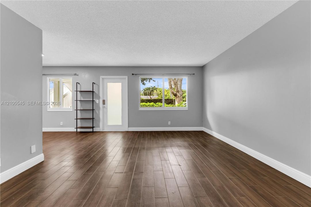 Wood-finish ceramic flooring, light grey painted walls, white baseboards, and multiple windows providing natural light