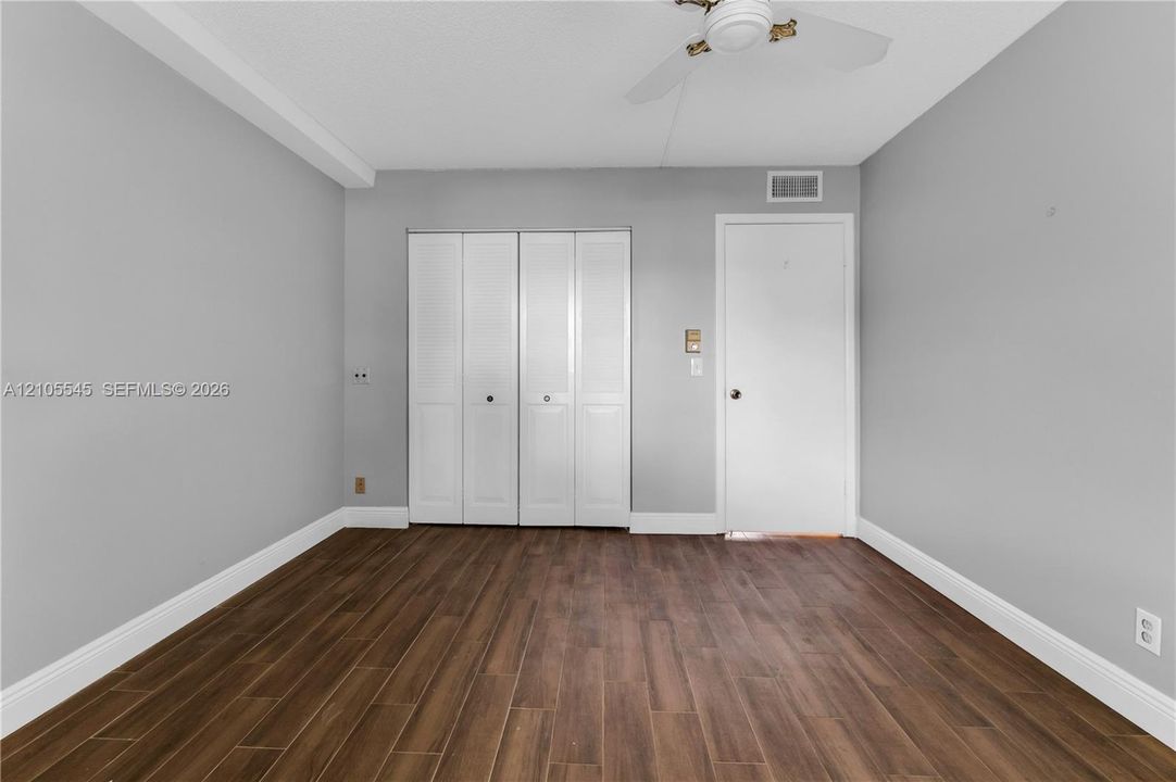 Wood-finish ceramic flooring, white bi-fold closet doors, ceiling fan, and light gray wall paint