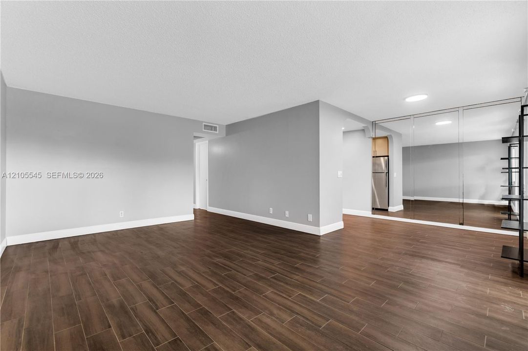 Spacious open-concept room featuring wood-finish tile flooring, light gray wall paint, and full wall mirrors