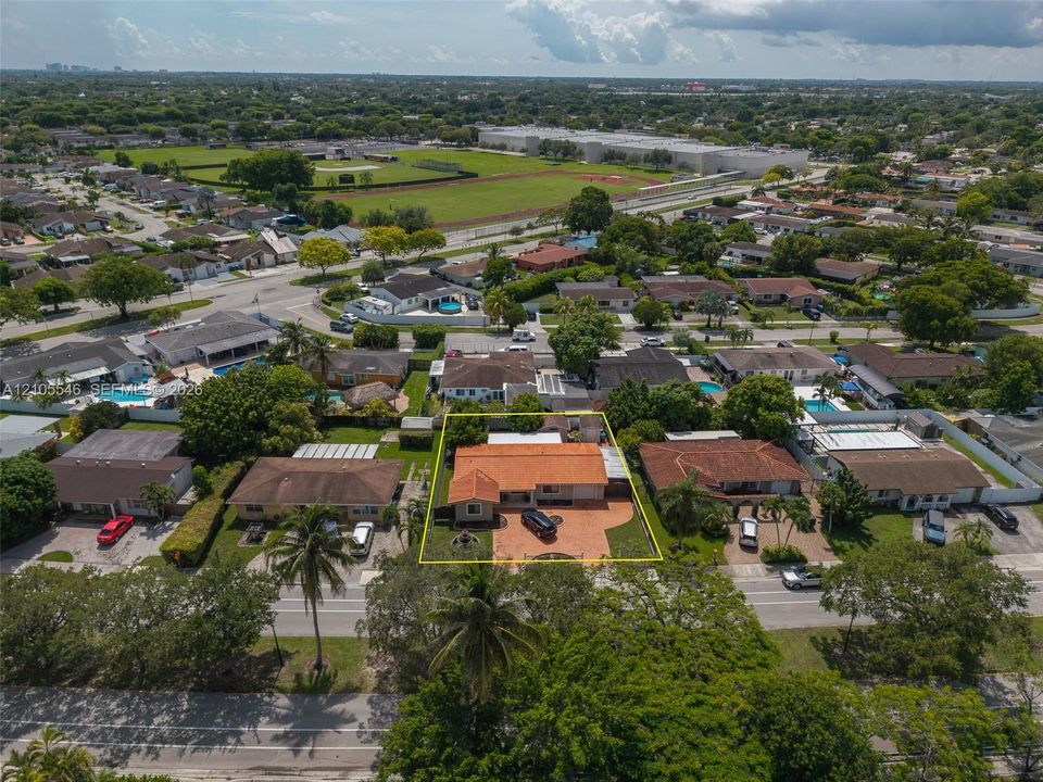 Aerial view of property featuring a tile roof, paved circular driveway, enclosed backyard, and mature landscaping