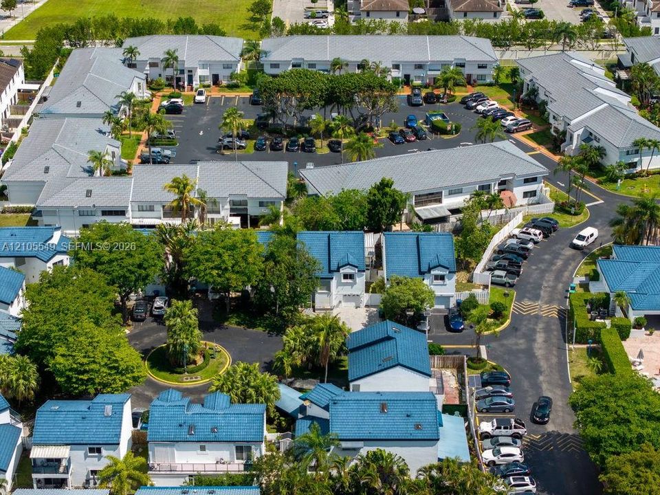 Aerial property overview featuring multiple residential buildings with varied roof styles, extensive paved parking areas, and mature landscaping