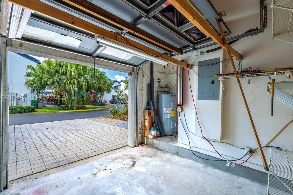 Garage interior with water heater, electrical panel, and fluorescent lighting