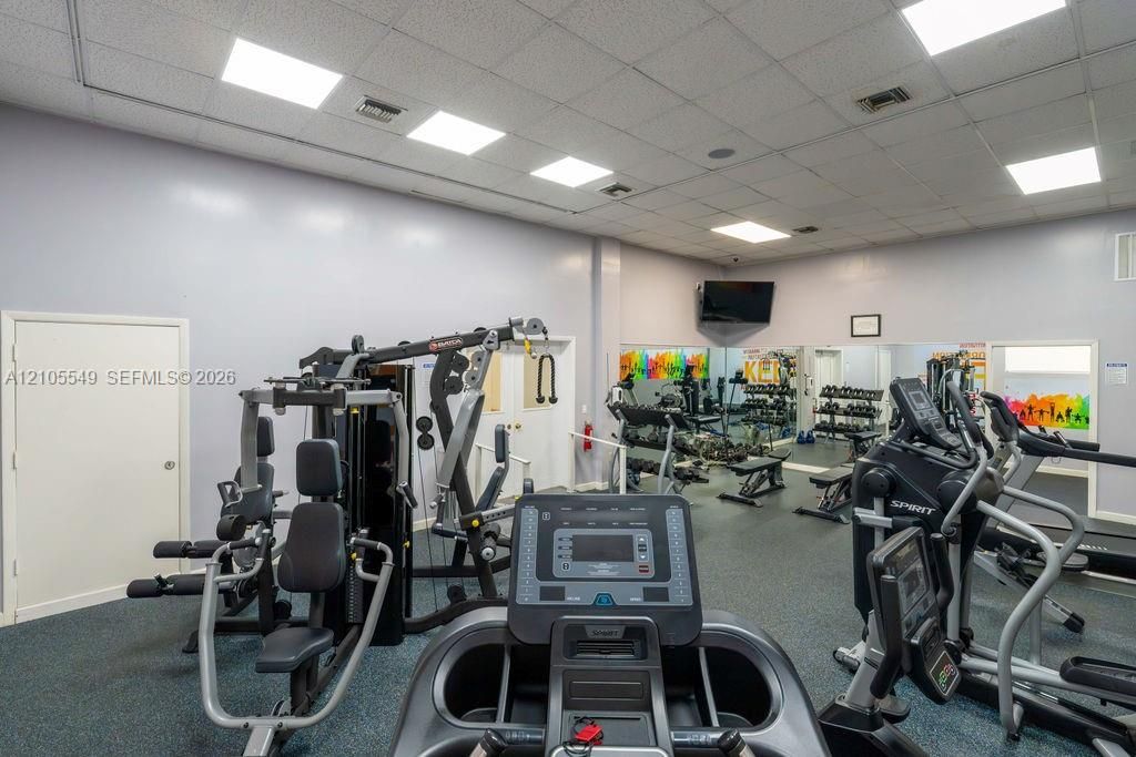 Dedicated fitness area featuring gym equipment, resilient flooring, recessed lighting, and a wall-mounted display
