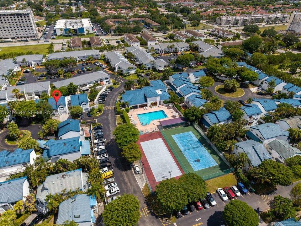 Community setting featuring multiple residential buildings with blue roofs, a swimming pool, and a tennis court