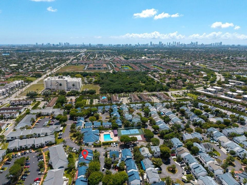 Aerial perspective showcasing urban and suburban development, prominent city skyline in the distance, community pool, and tennis court
