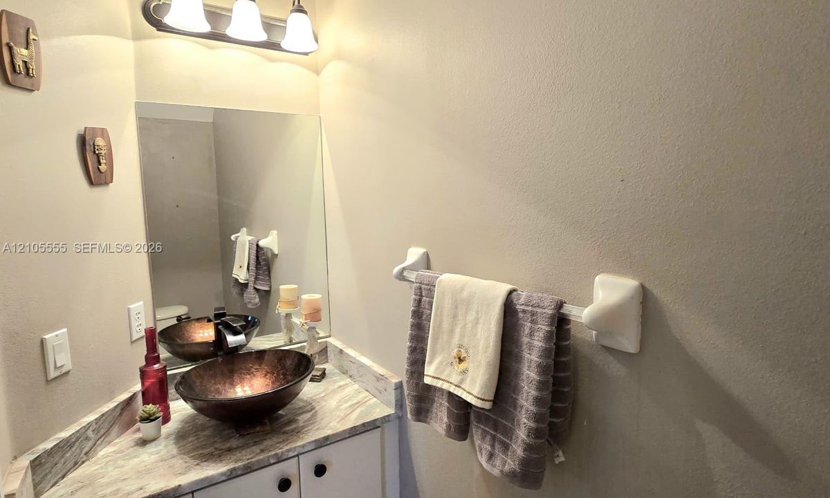 Corner vanity featuring a stone-patterned countertop, copper-tone vessel sink, white cabinetry, and a wall-mounted light fixture