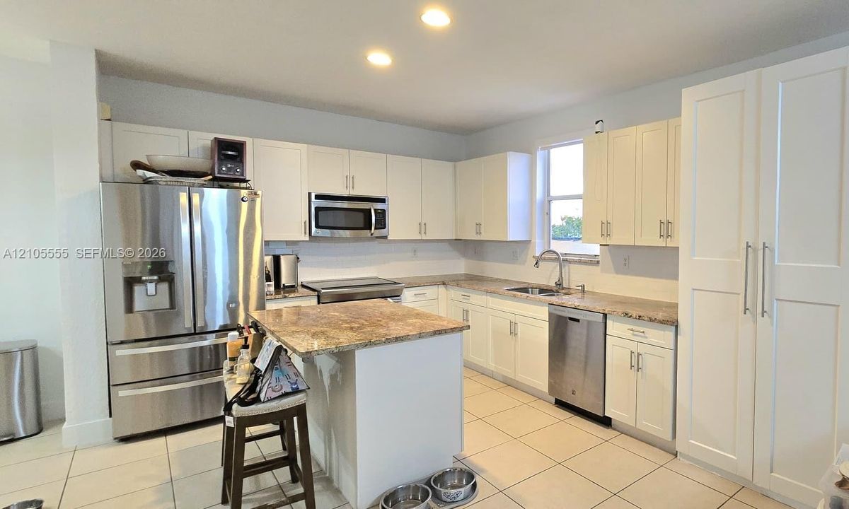 Kitchen featuring white shaker-style cabinetry, stone-finish countertops, stainless steel appliances, a center island, and tile flooring