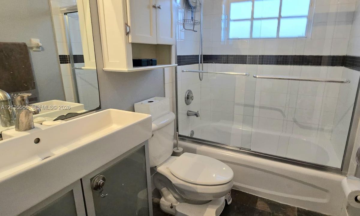 Bathroom featuring a rectangular vessel sink with a chrome faucet, wall-mounted cabinetry, a tub-shower combination with sliding glass doors, and tiled walls with a decorative accent border