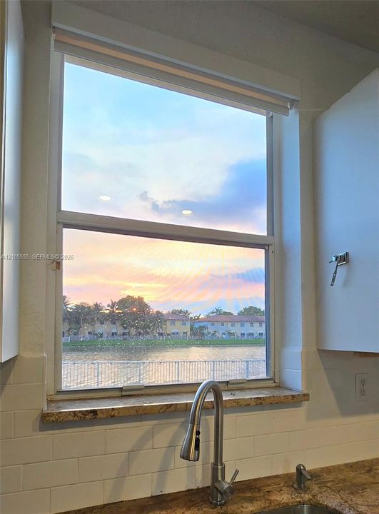 Single-hung window featuring a stone sill, stainless steel pull-down faucet, white subway tile backsplash, and water-front scenery