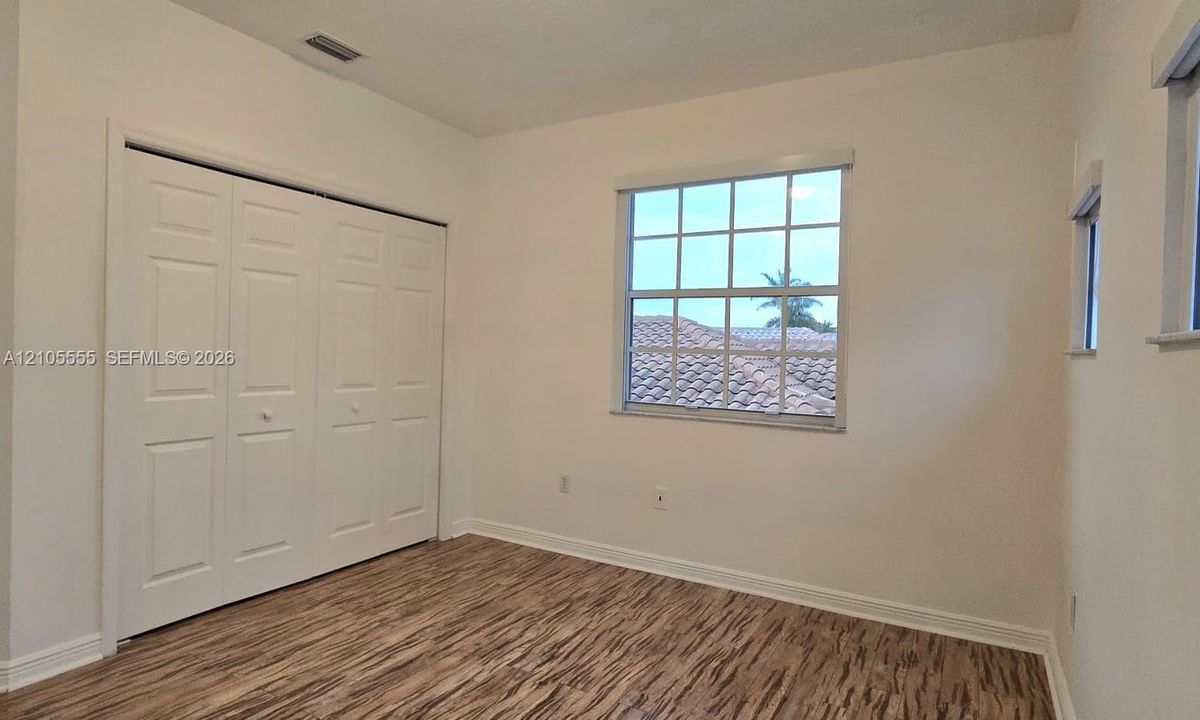 Interior room featuring wood-finish flooring, multi-pane window with exterior tile roof scenery, and a three-panel closet with dual doors