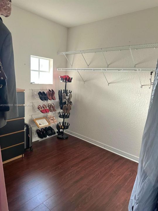 Walk-in closet featuring wood-finish flooring, white wall-mounted wire shelving, and a small rectangular window