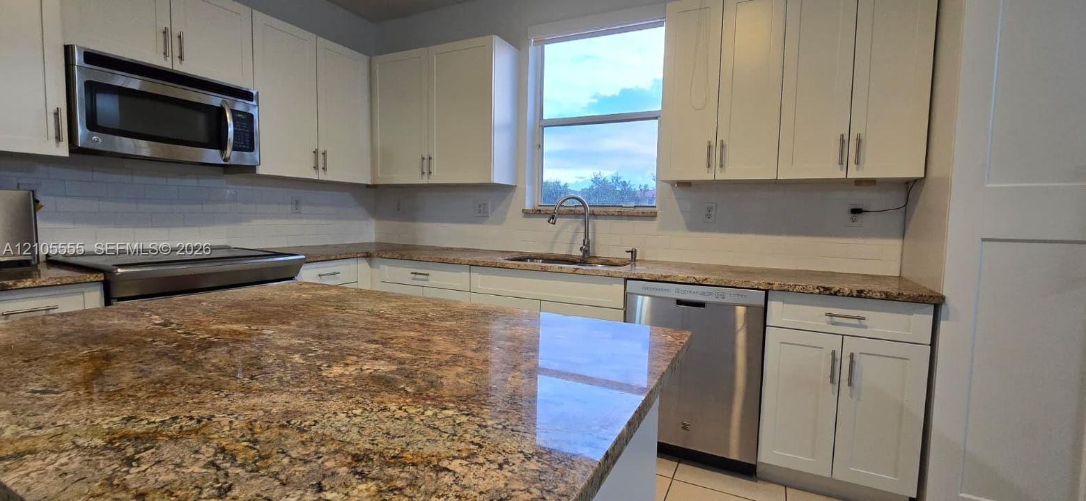 Kitchen featuring white cabinetry, stone countertops, stainless steel appliances, a subway tile backsplash, and a large center island